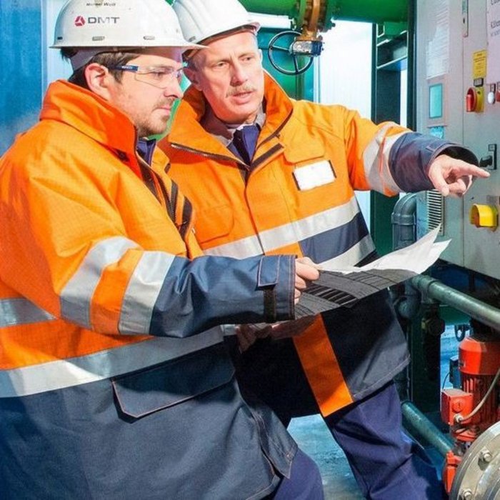 Arbeiter in Schutzausrüstung neben einer Industriemaschine, möglicherweise einer Pumpe oder einem Kompressor